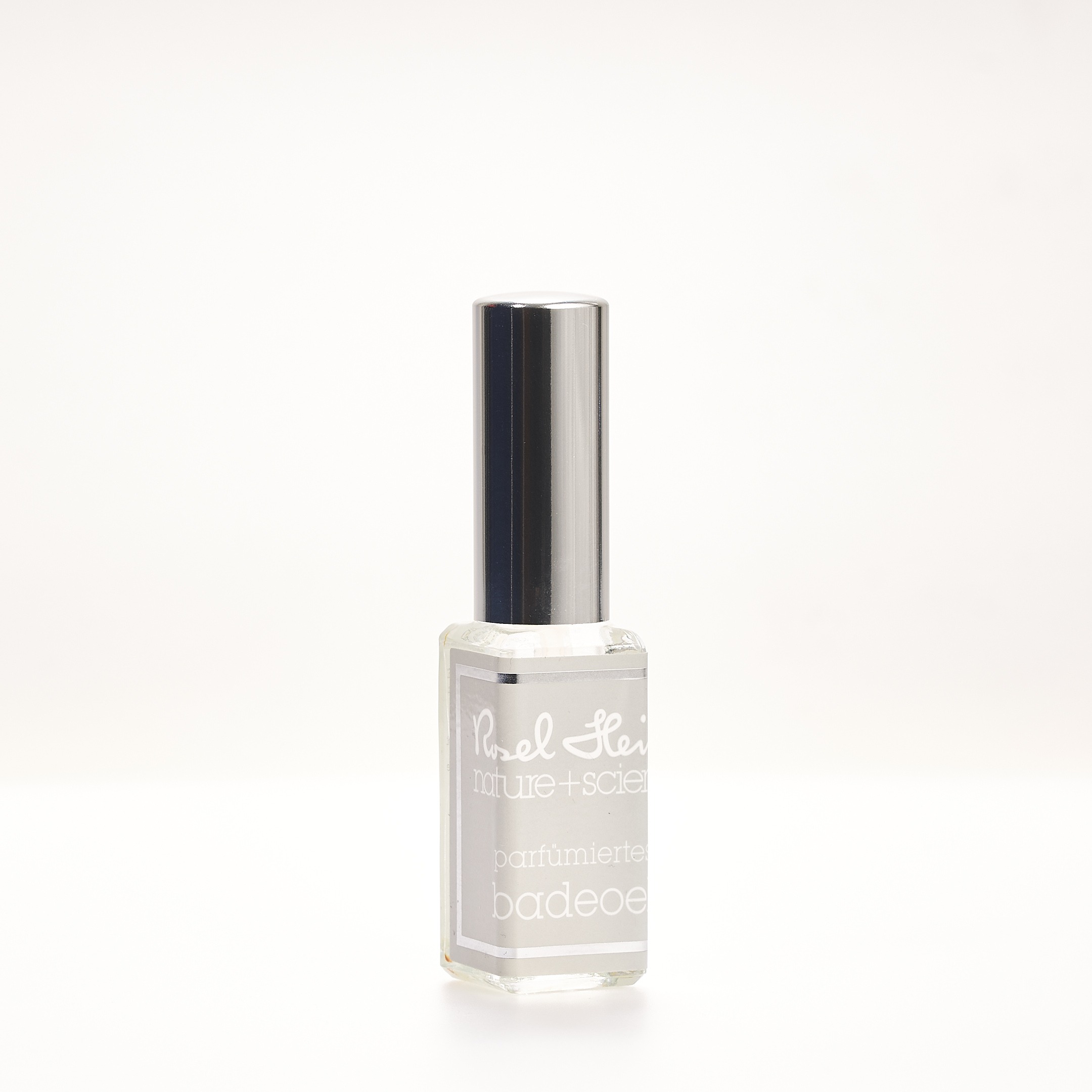 Eine kleine, klare Glasflasche mit silbernem Verschluss, die parfümiertes Badeöl enthält. Auf dem Etikett steht „Badeöl mini 10ml“. Der Hintergrund ist schlicht weiß.