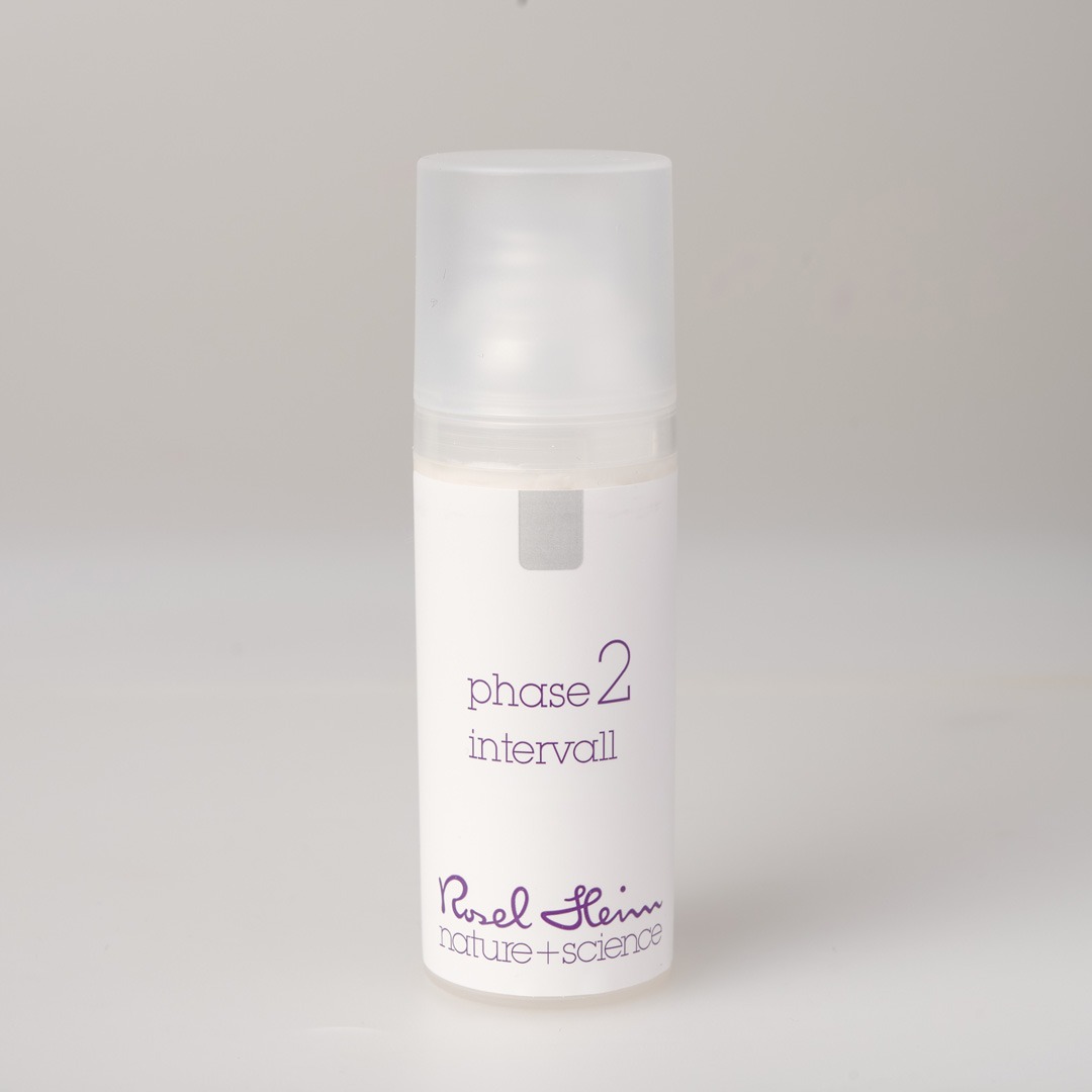 Eine kleine, zylindrische, weiße Flasche mit mattiertem Deckel und der Aufschrift „intervall Avocadoöl parfümfrei 50ml Phase 2“ in violetter Schrift. Der Produktaufdruck auf der Unterseite lautet „Ruel Heim nature + science“. Die Flasche steht auf einem schlichten, hellgrauen Hintergrund.